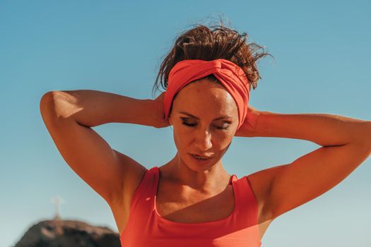 sport outdoor photo of beautiful young brunette woman in black sport suit with headband smiling and listening to music on headphones by the sea