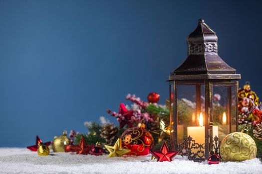 Burning Christmas lantern and fir tree decor in snow over blue background with copy space