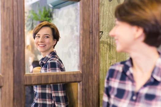 Young woman looking in a mirror. The mirror reflects her smiling face. Natural beauty and female.