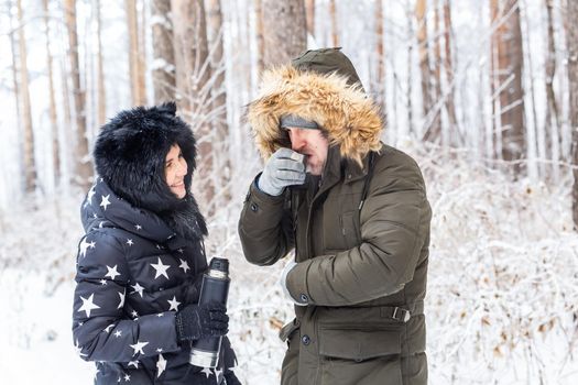 Season and walk concept - Happy couple drinking hot tea in winter forest.