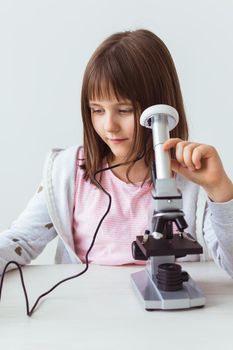 Schoolgirl using microscope in science class. Technologies, lessons and children.