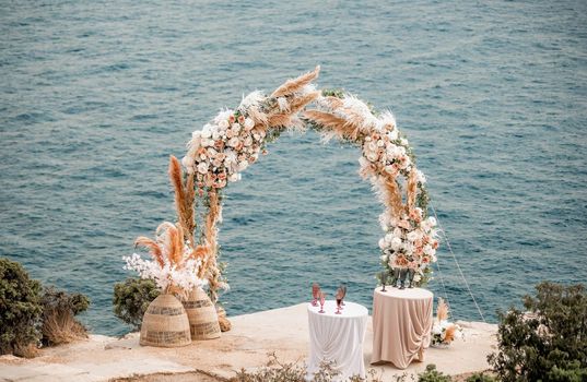 Elegant and stylish arch wedding ceremony on the sea. The round wedding arch is decorated with a variety of flowers. Place for text. The concept of calmness silence and unity with nature.