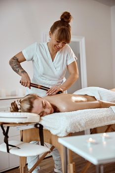 Professional confident massage master is doing procedures to caucasian woman in minimalistic modern cabinet