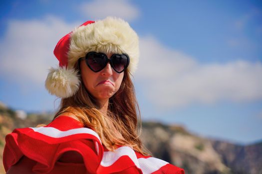 Young brunette woman in red swimsuit and Santa hat, swimming on kayak around basalt rocks like in Iceland. Back view. Christmas and travel concept