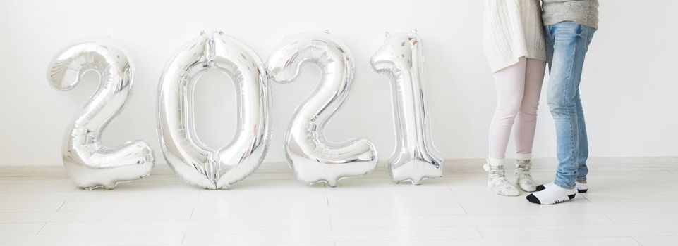 Holidays, festive and party concept - Happy loving couple holds silver 2021 balloons on white background. New Year celebration