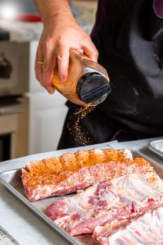 The hand of a male chef puts salt and spices on the raw piece of beef ribs meat. Raw St Louis Style BBQ Ribs preparation process