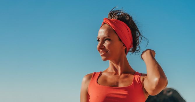 sport outdoor photo of beautiful young brunette woman in black sport suit with headband smiling and listening to music on headphones by the sea
