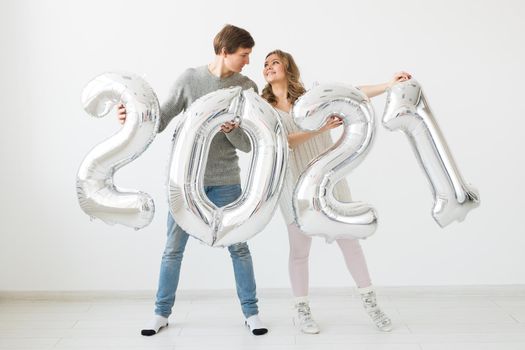 Holidays, festive and party concept - Happy loving couple holds silver 2021 balloons on white background. New Year celebration