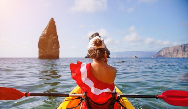 Young brunette woman in red swimsuit and Santa hat, swimming on kayak around basalt rocks like in Iceland. Back view. Christmas and travel concept