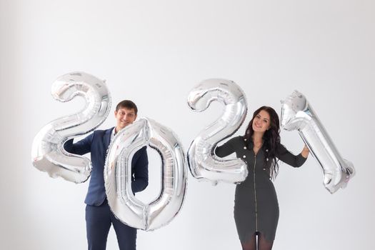 New year, celebration and holidays concept - love couple having fun with sign 2021 made of silver balloons for new year on white.