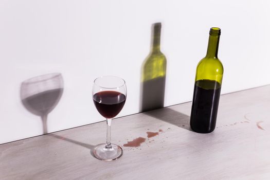 Bottle with wine and glass, red puddle of wine on the table. Cleaning after party concept