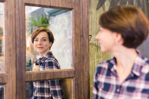 Young woman looking in a mirror. The mirror reflects her smiling face. Natural beauty and female.