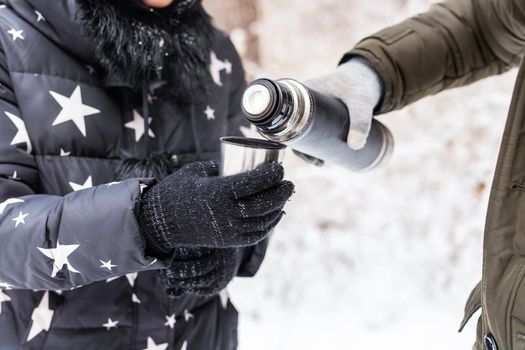 Thermos and cold season concept - A woman pours a hot drink. Couple on a winter holiday.