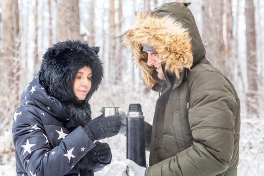 Season and walk concept - Happy couple drinking hot tea in winter forest.