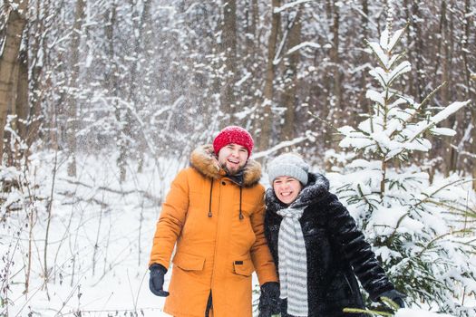 Love, season, friendship and people concept - happy young man and woman having fun and playing with snow in winter forest.