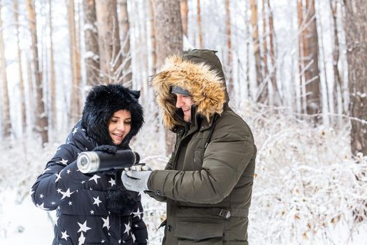 Young couple in love drink a hot drink from a thermos and enjoy winter nature