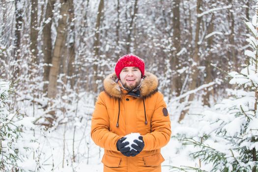 Young man throwing snow in winter forest. Guy having fun outdoors. Winter activities