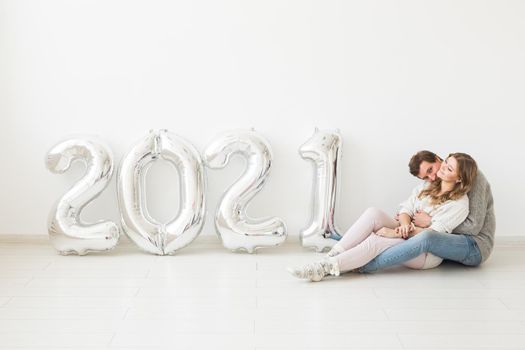 Holidays, festive and party concept - Happy loving couple holds silver 2021 balloons on white background. New Year celebration