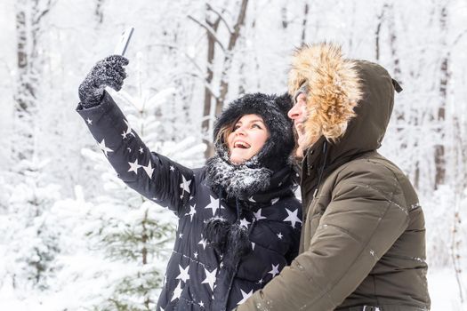 Season, love, technology and leisure concept - happy couple taking selfie by smartphone over winter.