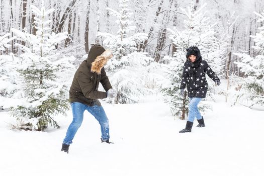 Lifestyle, season and leisure concept - Funny couple playing snowball in winter park.