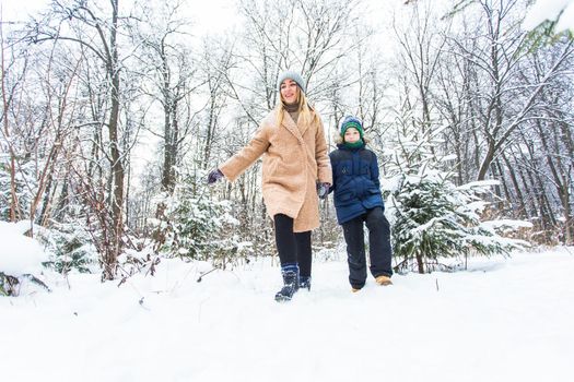 Parenting, fun and season concept - Happy mother and son having fun and playing with snow in winter forest.