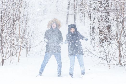 man and woman having fun and playing with snow in winter forest