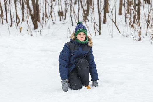 Young boy plays with snow, have fun, smiles. Teenager in winter park. Active lifestyle, winter activity, outdoor winter games, snowballs.