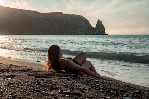 Selective focus. Happy carefree sensual woman with long hair in black swimwear posing at sunset beach. Silhouette of young beautiful playful positive woman outdoor. Summer vacation and trip concept.