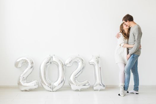 Holidays, festive and party concept - Happy loving couple holds silver 2021 balloons on white background. New Year celebration