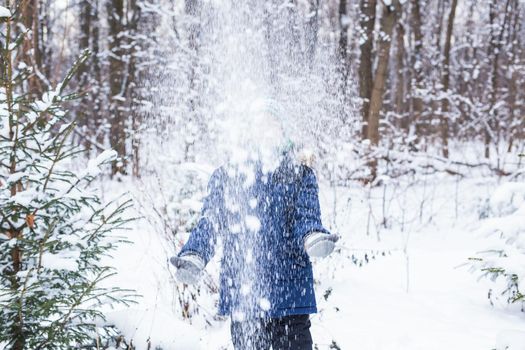 Young boy plays with snow, have fun, smiles. Teenager in winter park. Active lifestyle, winter activity, outdoor winter games, snowballs.