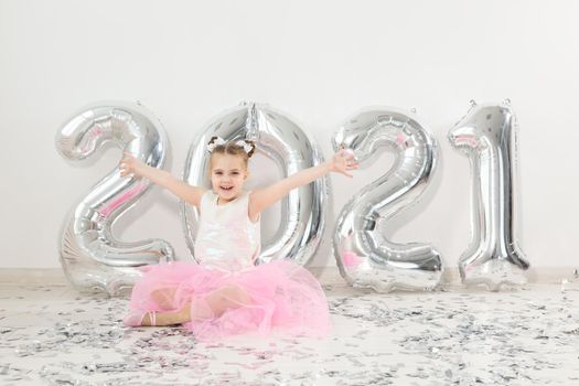 New year, holidays and celebration concept - Little girl sitting near with numbers balloons 2021