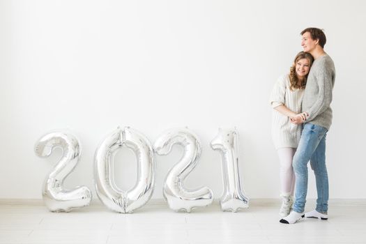 Holidays, festive and party concept - Happy loving couple holds silver 2021 balloons on white background. New Year celebration