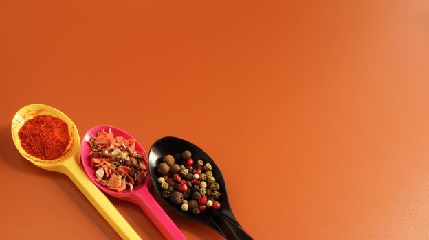 Various spices in plastic spoons on a brown background. Copy space. A mixture of peppers, red smoked paprika, seasoning twelve vegetables