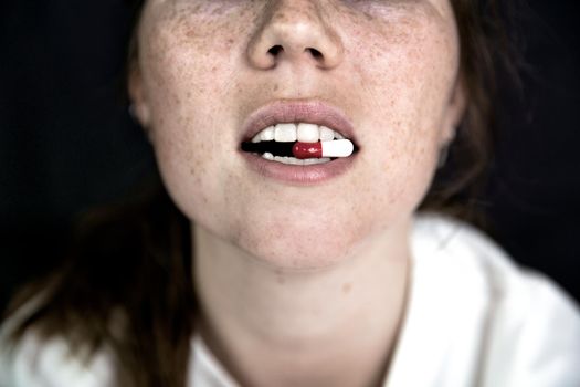 Young woman,teenager with Capsule on tong on dark black background, taking pills. medicine,drugs,health concept close up portrait