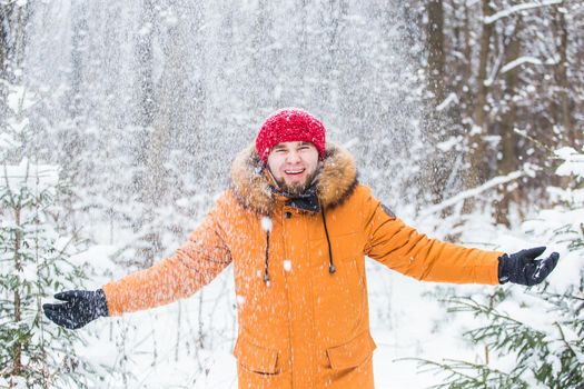 Young man throwing snow in winter forest. Guy having fun outdoors. Winter activities