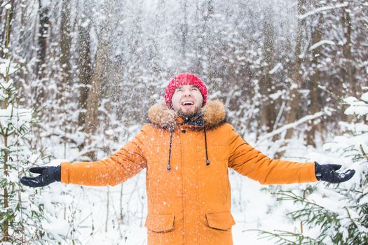 Young man throwing snow in winter forest. Guy having fun outdoors. Winter activities