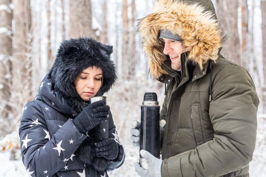 Young couple in love drink a hot drink from a thermos and enjoy winter nature