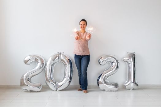 New Year celebration and party concept - Happy young woman with sparklers near silver 2021 balloons on white background