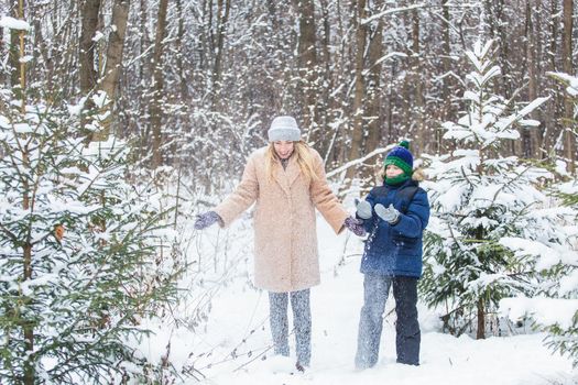 Parenting, fun and season concept - Happy mother and son having fun and playing with snow in winter forest.