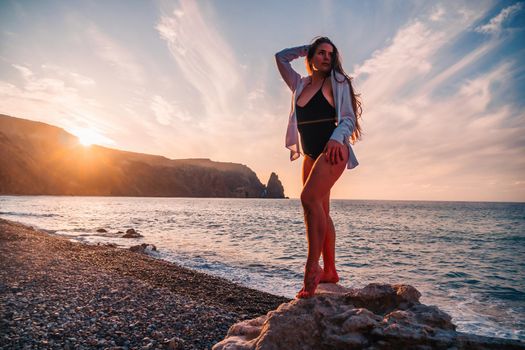 Selective focus. Happy carefree sensual woman with long hair in black swimwear posing at sunset beach. Silhouette of young beautiful playful positive woman outdoor. Summer vacation and trip concept.