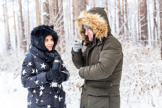 Young couple in love drink a hot drink from a thermos and enjoy winter nature
