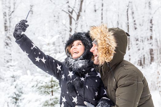 Technologies and relationship concept - Happy smiling couple taking a selfie in a winter forest outside.