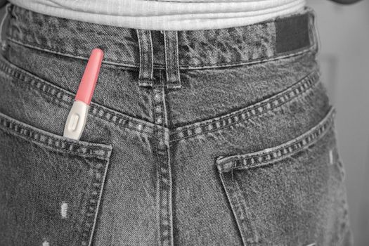 Young woman with positive pregnancy test in pocket of jeans close-up motherhood happiness modern retro background