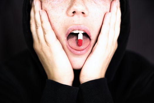 A woman is holding a pill, capsule with a drug on her tongue, teenager taking xtc.cocaine or other drugs or medicine dark background