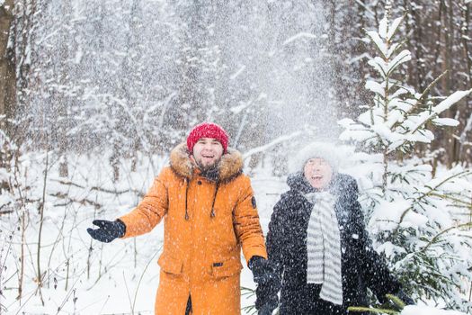 Love, season, friendship and people concept - happy young man and woman having fun and playing with snow in winter forest.