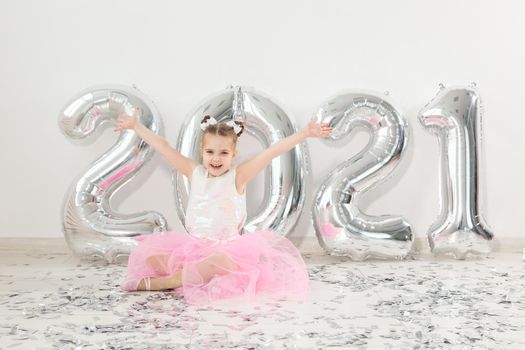 New year, holidays and celebration concept - Little girl sitting near with numbers balloons 2021