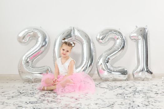 New year, holidays and celebration concept - Little girl sitting near with numbers balloons 2021