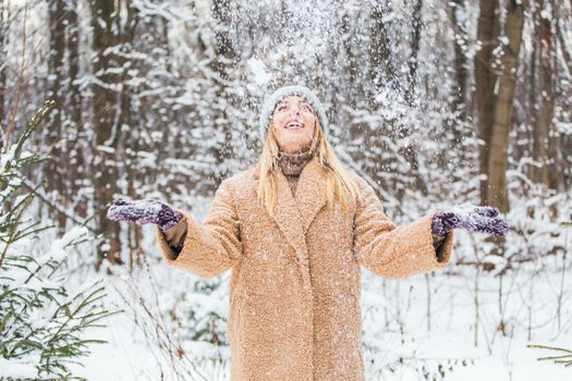 Young woman throwing snow in the air at sunny winter day, she is happy and fun