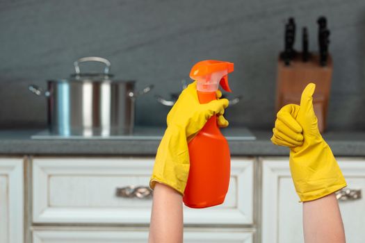 Hands in yellow gloves against blurred kitchen background. Housekeeping concept