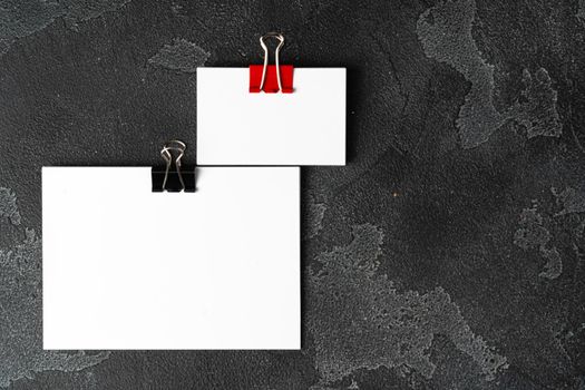 White businesscards united with a paper clip on a black rough background, copy space